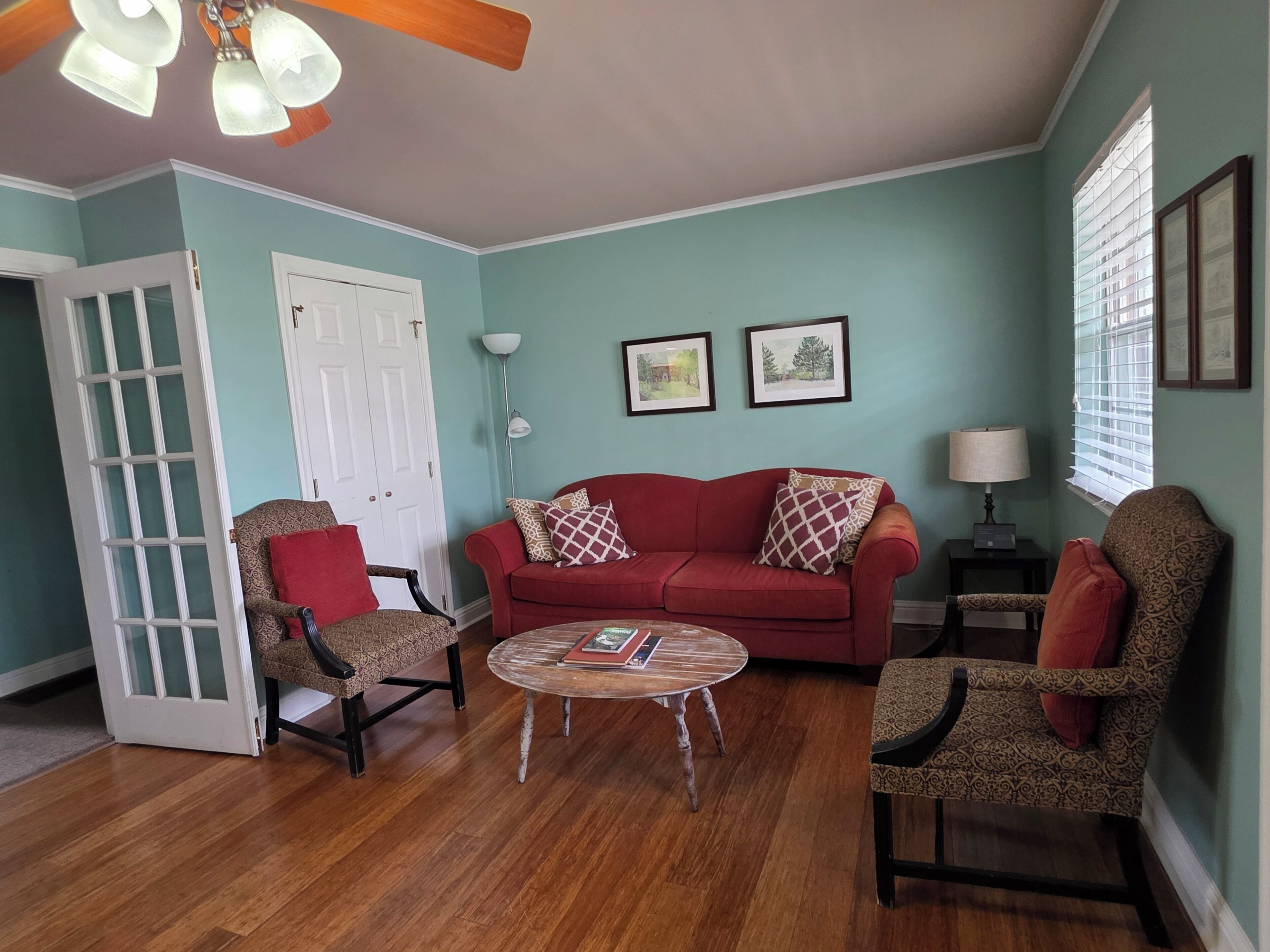 A living room with a red sofa, patterned armchairs, a coffee table, and a ceiling fan.