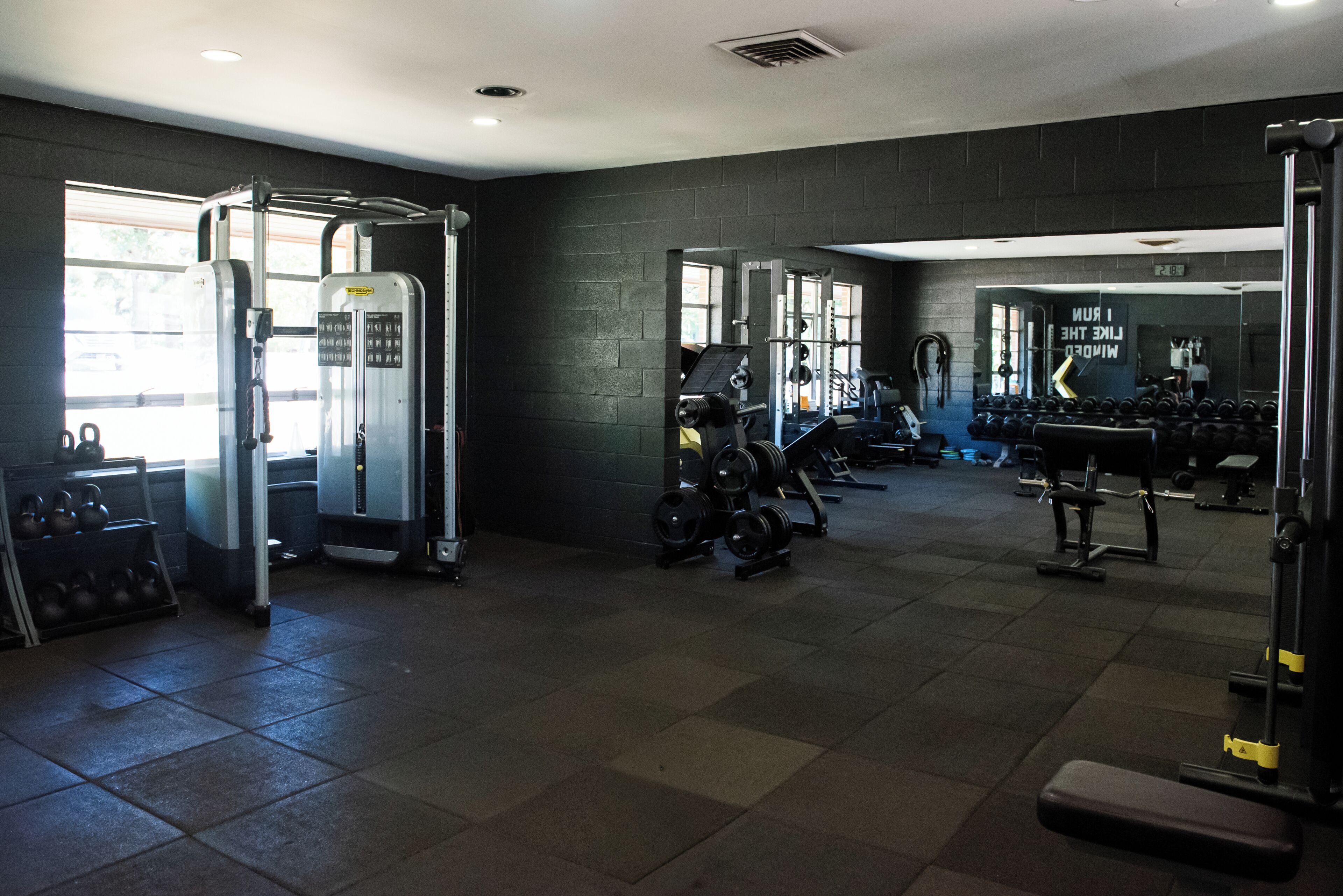 Un gimnasio con equipo de levantamiento de pesas, cintas de correr y un espejo.