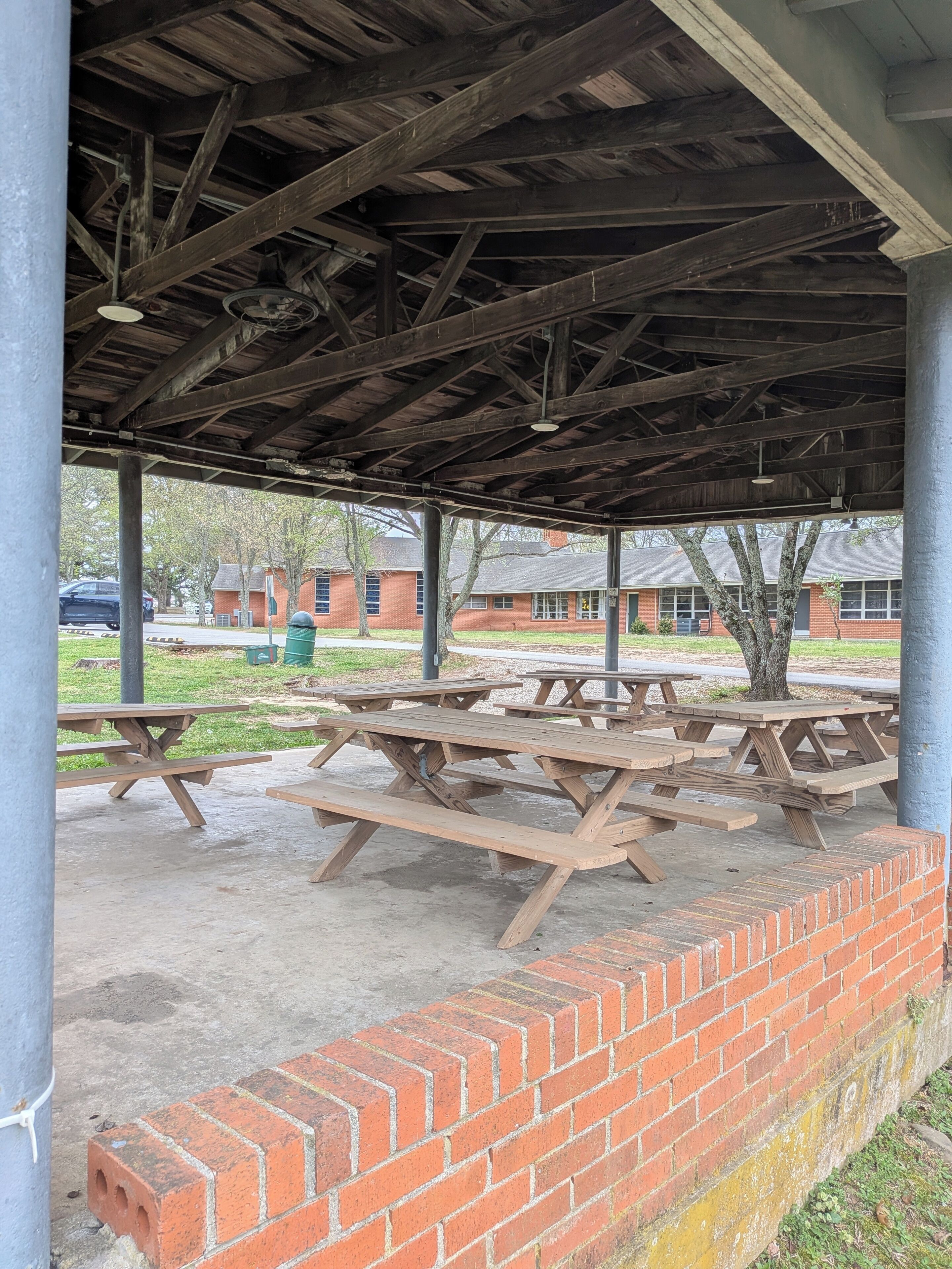 Un área de picnic techada al aire libre con mesas de madera y un muro de ladrillo.