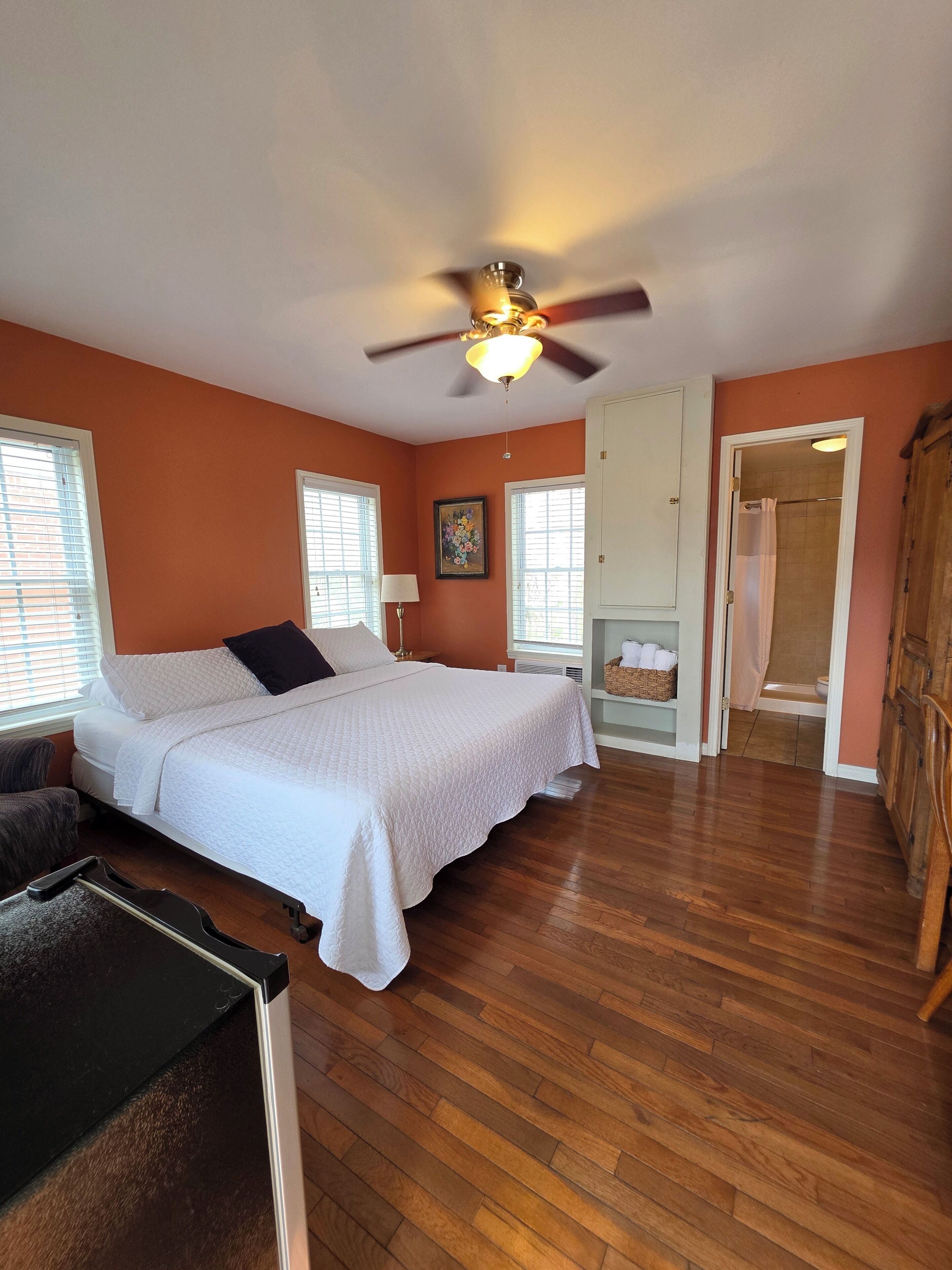 A bedroom with a bed, a ceiling fan, a window, and a door leading to a bathroom.