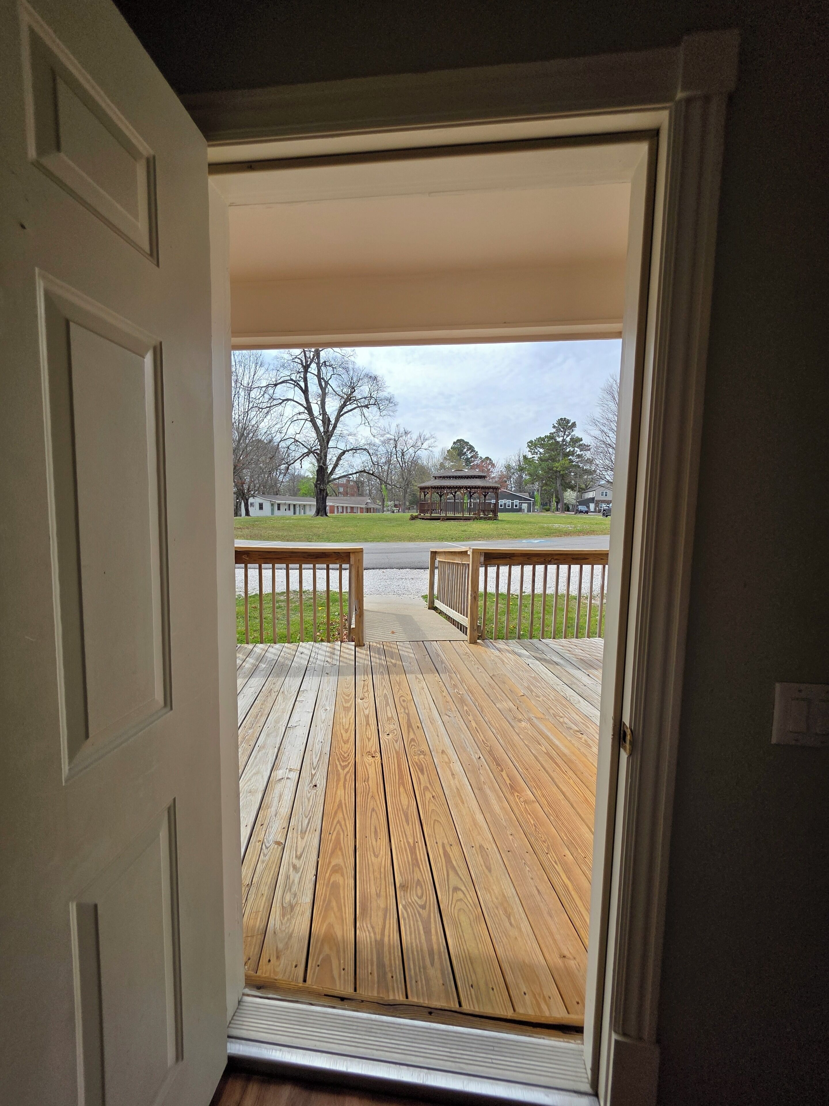 A wooden deck with a railing, leading to a gazebo in a park.