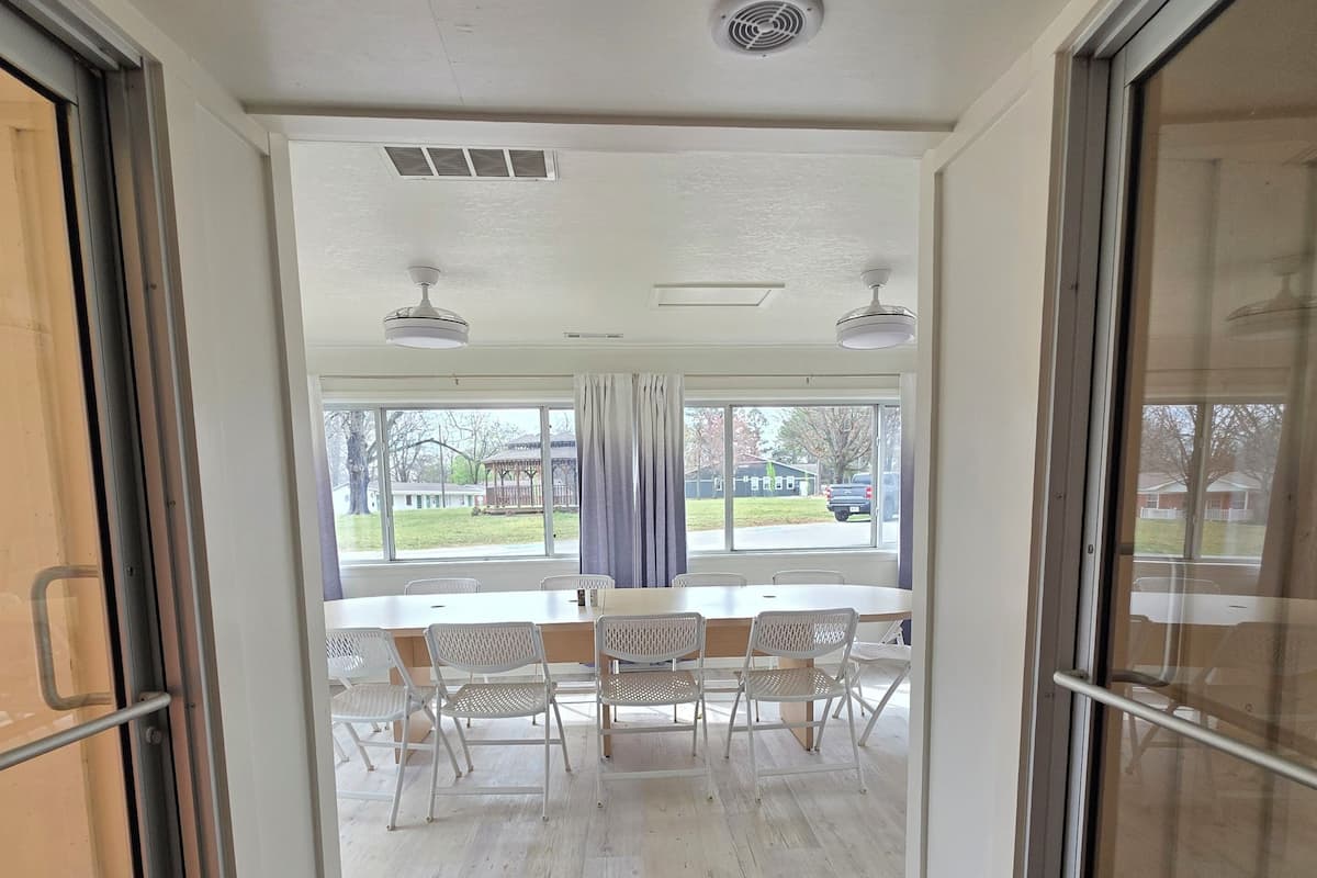 An interior view of a hotel room with a sliding glass door leading to a balcony, a black doormat, and a ceiling fan.