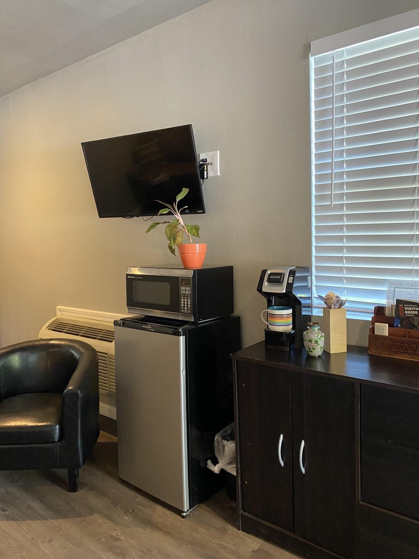 A compact kitchenette with a microwave, a small refrigerator, a coffee maker, and a potted plant.