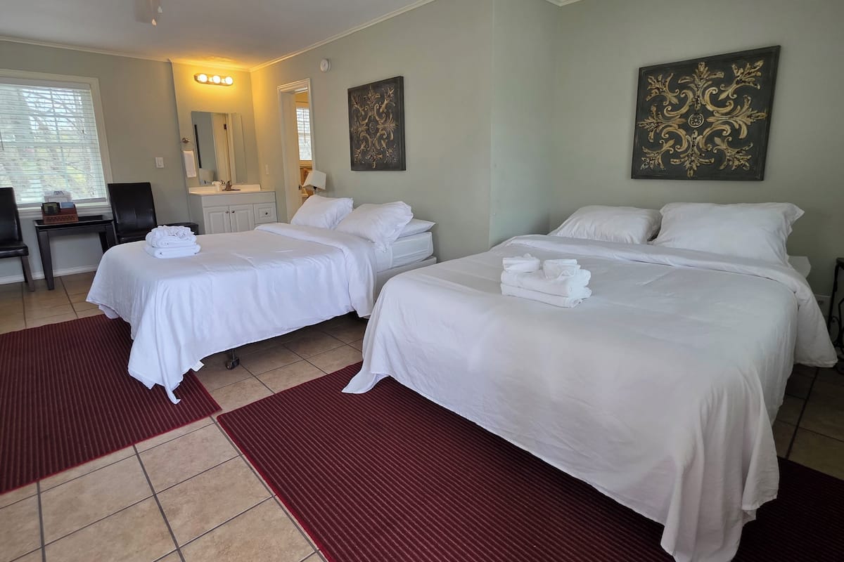 A hotel room with two beds, a desk, a chair, a mirror, and artwork on the walls.