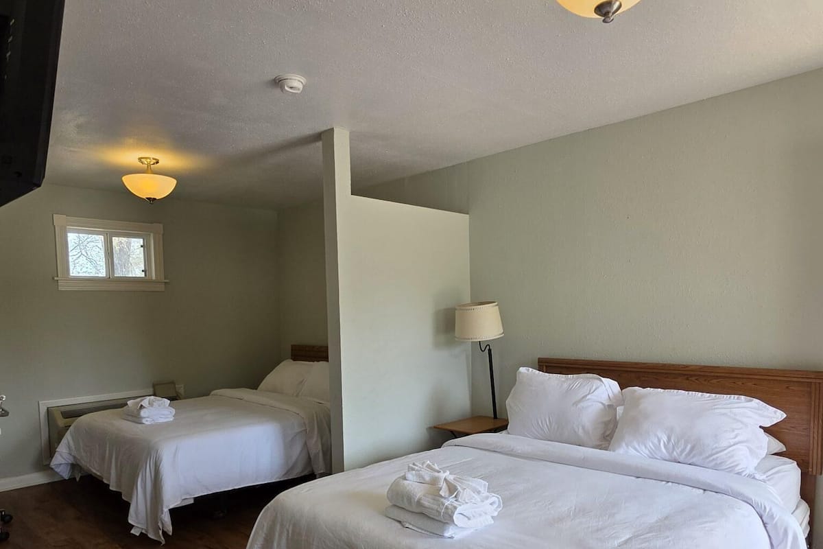 A hotel room with two beds, a television, a window, and a ceiling light fixture.