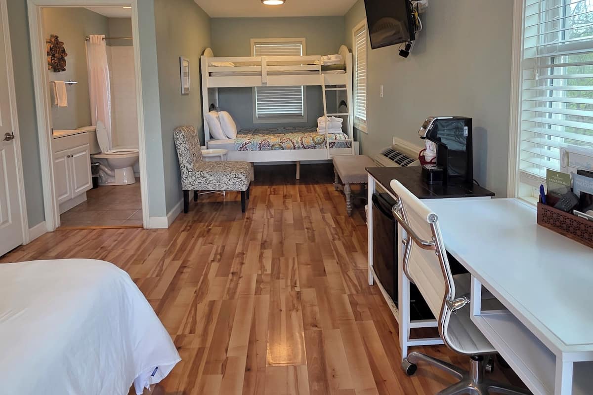 A bedroom with a bunk bed, a desk, a chair, a television, and a window with blinds.