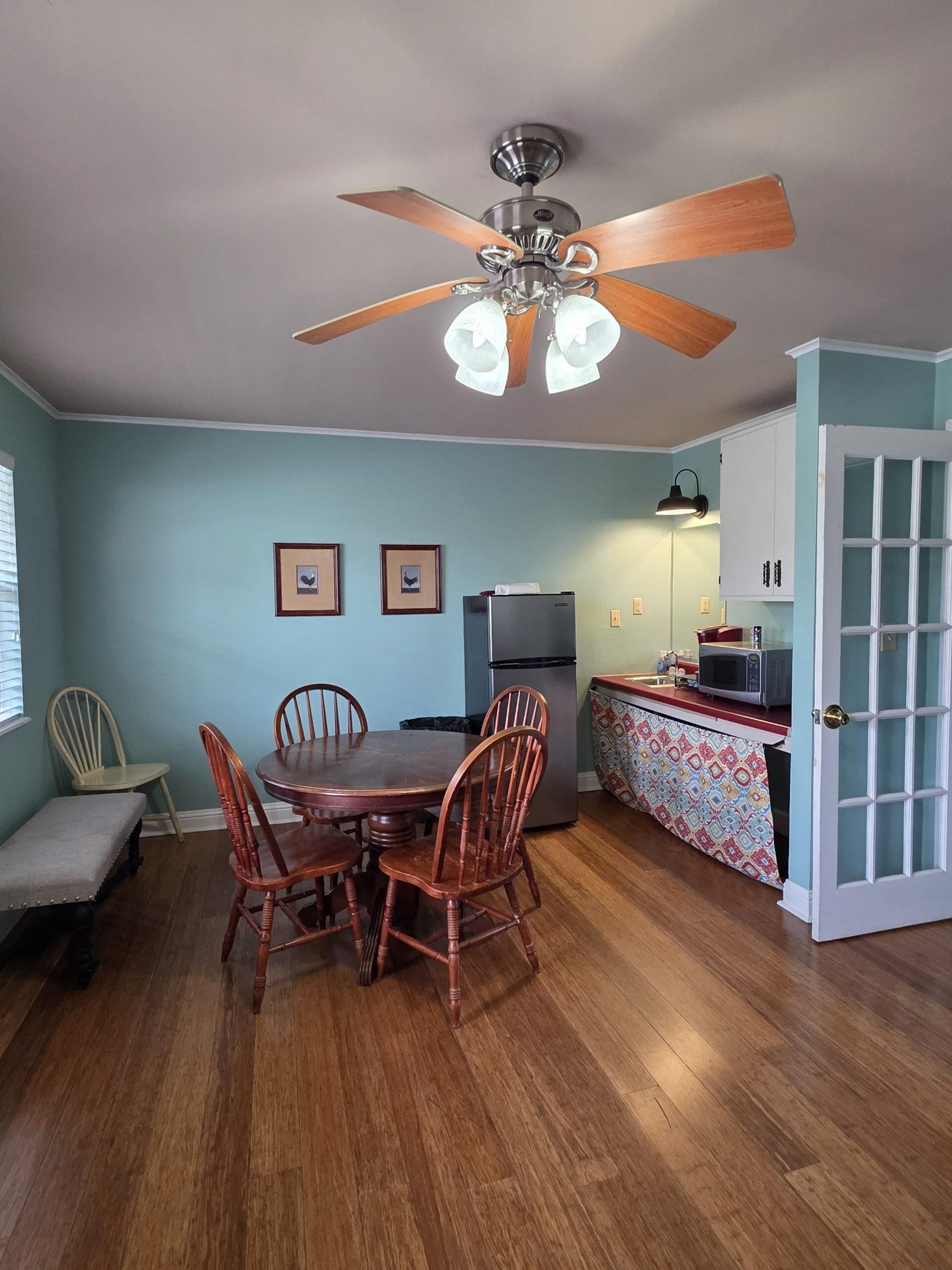 A kitchen with a dining table, chairs, a ceiling fan, a refrigerator, and a microwave.