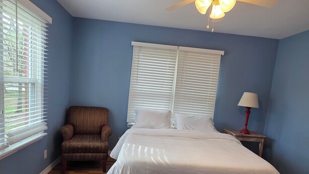 A bedroom with a bed, a chair, a nightstand, and a ceiling fan. - Mount Sequoyah Center (Fayetteville)