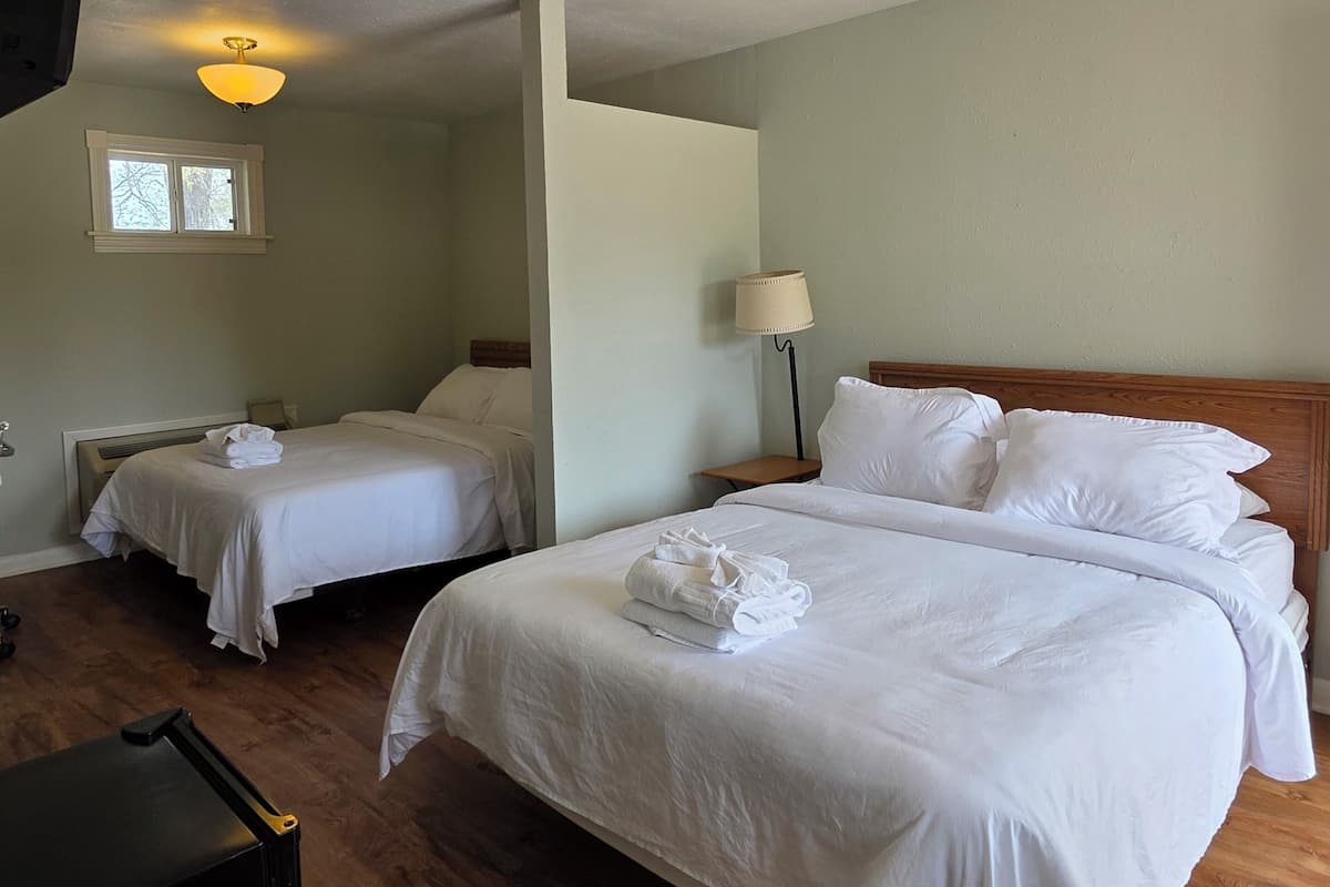 A hotel room with two beds, a TV, a window, and a lamp.