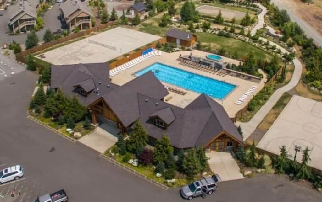 Une grande maison avec une piscine, un terrain de basket et une allée où sont garées des voitures.
