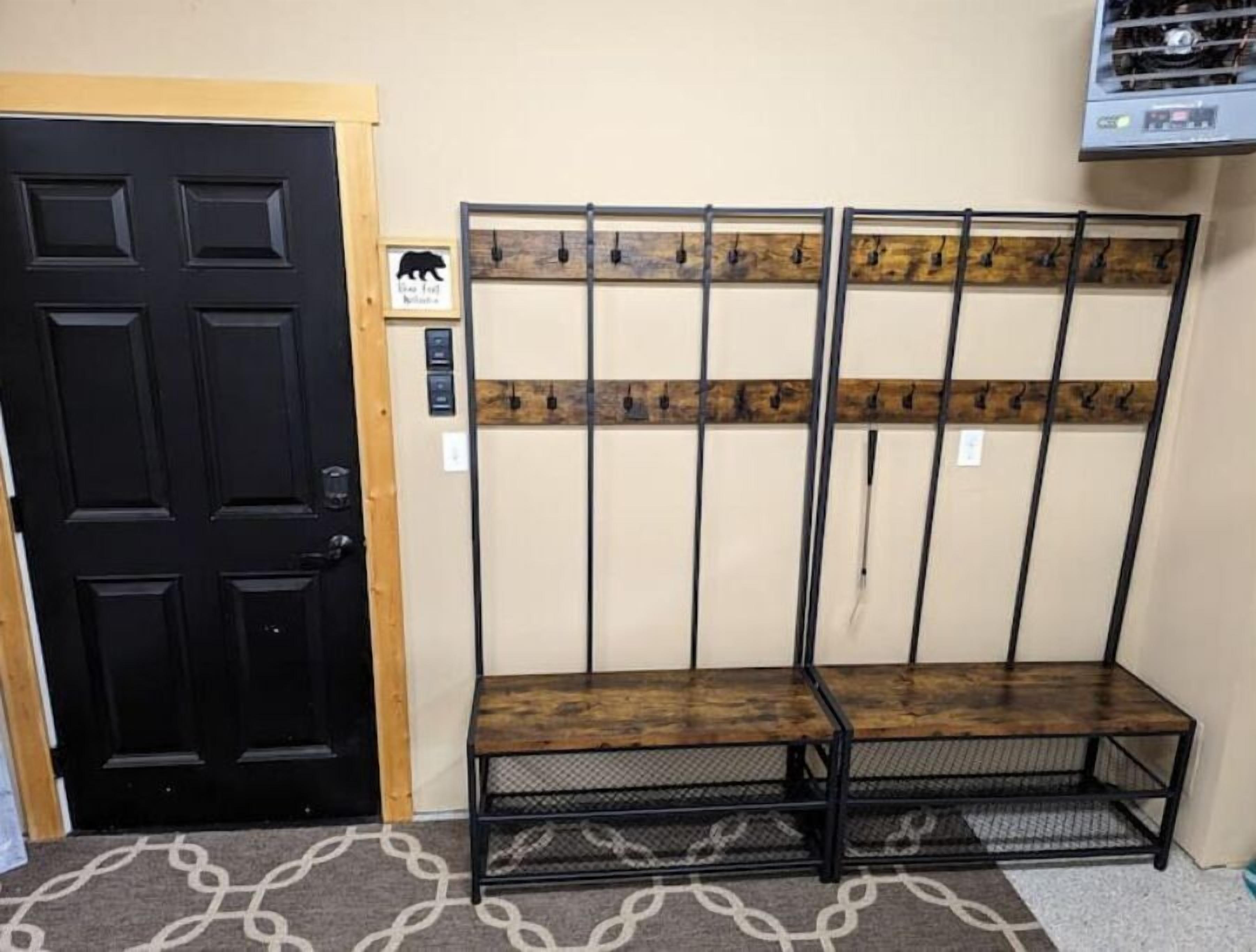 A room with a black door, a bench with a wooden top, and a wall-mounted rack with hooks.