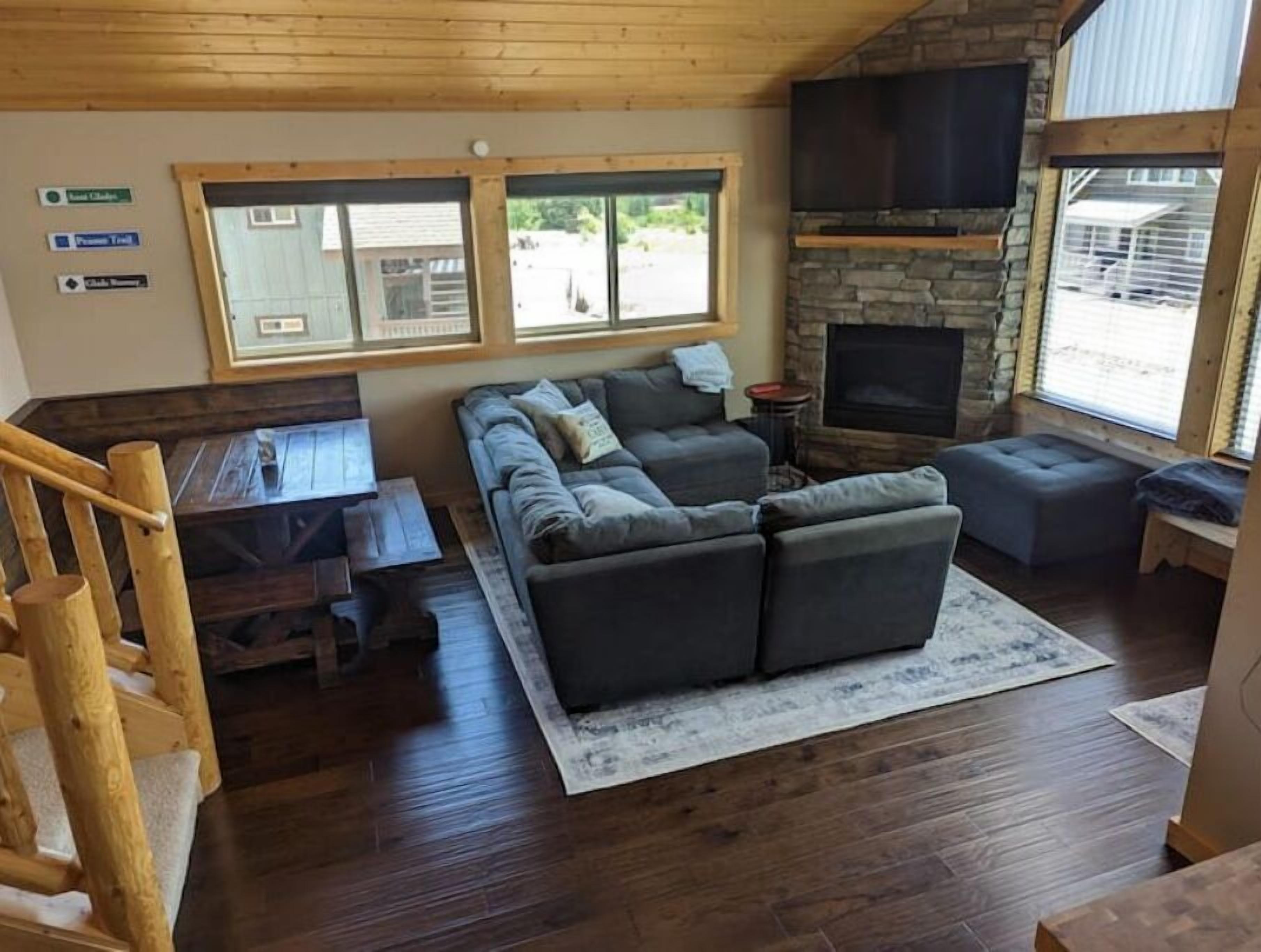 A cozy living room with a stone fireplace, a sectional sofa, and a wooden staircase.