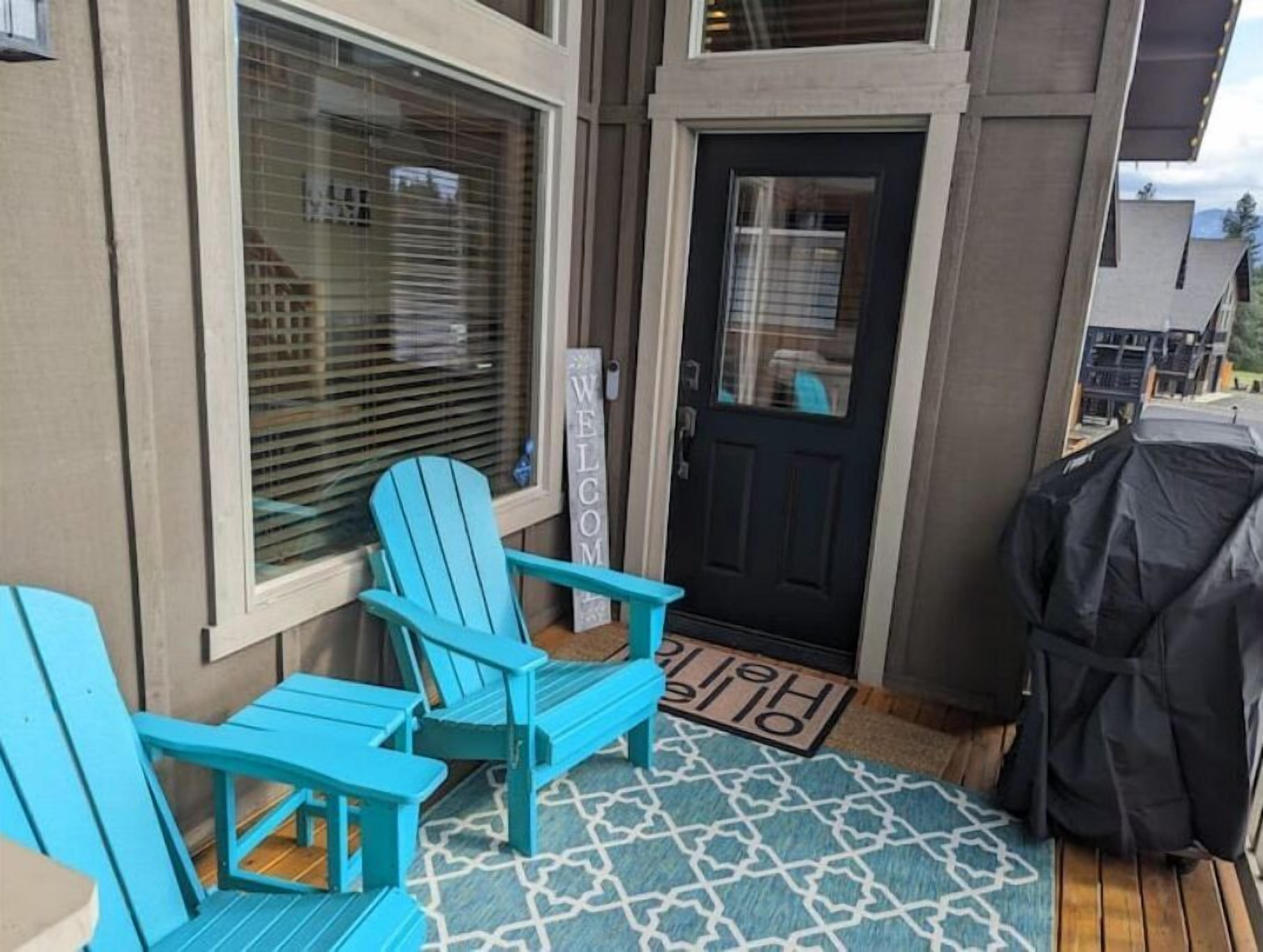 Un espace extérieur abrité avec deux fauteuils Adirondack turquoise, un barbecue noir et un paillasson.