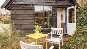 Une cabane en bois dotée d’un petit patio avec une table jaune et des chaises blanches.