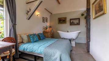 A bedroom with a bed, a wooden chair, a dresser, a vanity with a mirror, and a bathtub.