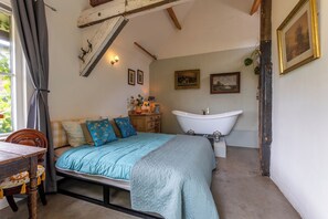 Ein Schlafzimmer mit einem Bett, einem Holzstuhl, einem Schminktischchen, einer Kommode und einer Badewanne.