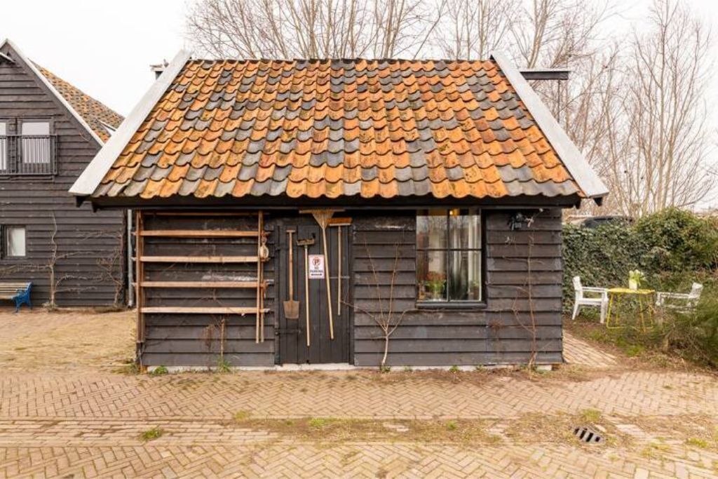 Ein kleines Holzgebäude mit einem Ziegeldach, einer schwarzen Tür und einem Fenster.
