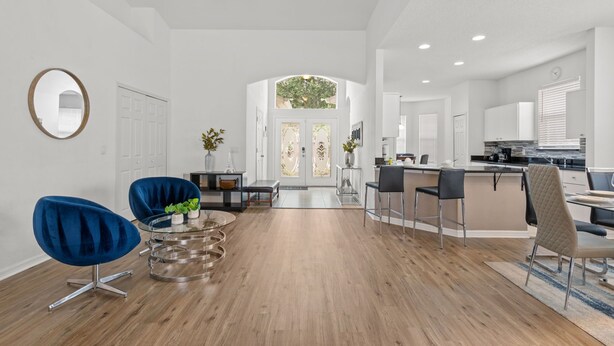 Amplia sala de estar con piso de madera, comedor con mesa de vidrio y cocina con gabinetes blancos.