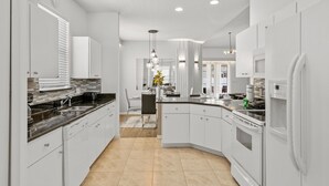 Una cocina moderna con armarios blancos, una isla central y un comedor visible al fondo.