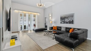 Un salón moderno con un sofá de cuero negro, una mesa de centro de vidrio y un cuadro de paisaje urbano en la pared.