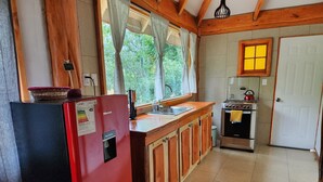 Une cuisine de taille réduite avec un réfrigérateur rouge, une cuisinière et des armoires en bois.