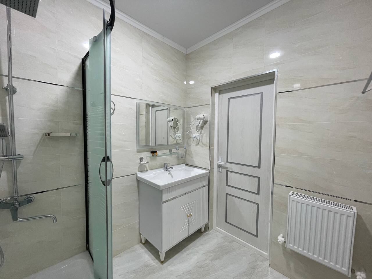 A bathroom with a glass shower enclosure, a white sink with a mirror, and a radiator.