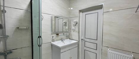 A bathroom with a glass shower enclosure, a white sink with a mirror, and a radiator.