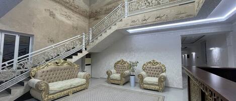 A grand interior with a staircase, ornate sofas, and a reception desk.