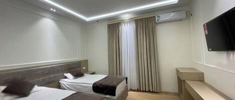 Habitación de hotel con dos camas, un televisor de pantalla plana montado en la pared y piso de madera.