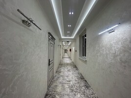 Un pasillo largo y estrecho con piso texturizado, iluminación empotrada y barandilla a la izquierda.