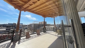 A balcony with a wooden ceiling, glass railings, and a view of buildings in the background. - Anor Qal'a (Khiva)