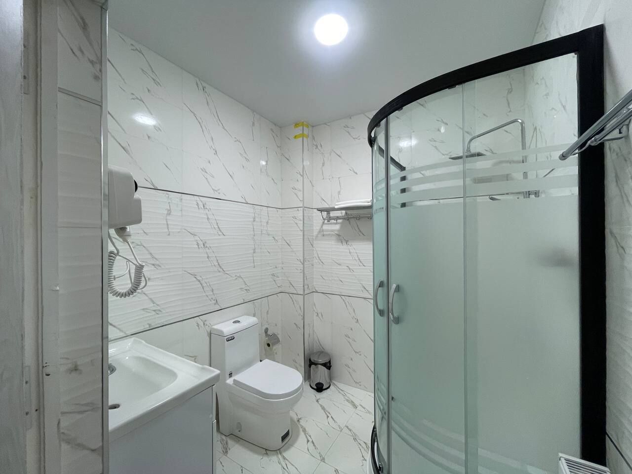 Un baño moderno con cabina de ducha de vidrio, inodoro blanco y lavamanos.