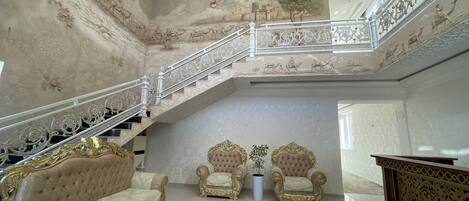 A grand room with a staircase, ornate chairs, and a luxurious sofa.