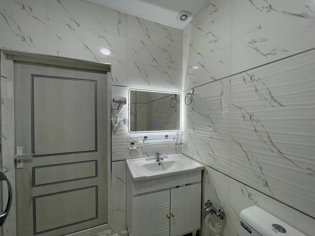 Un baño con pared de azulejos de mármol, un lavamanos con espejo y un inodoro.