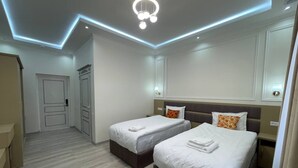 A hotel room with two beds, a wooden floor, a modern ceiling light, and a door in the background. - Anor Qal'a (Khiva)