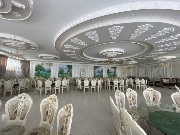 Un salón de banquetes con elaborados diseños en el techo, sillas blancas y una mesa verde.