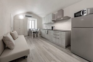 Una cocina moderna con microondas integrado, un área de comedor con mesa y sillas, y un sofá con cojines.