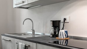 Une cuisine moderne avec un évier en acier inoxydable, une machine à café et une tasse posée sur le plan de travail.