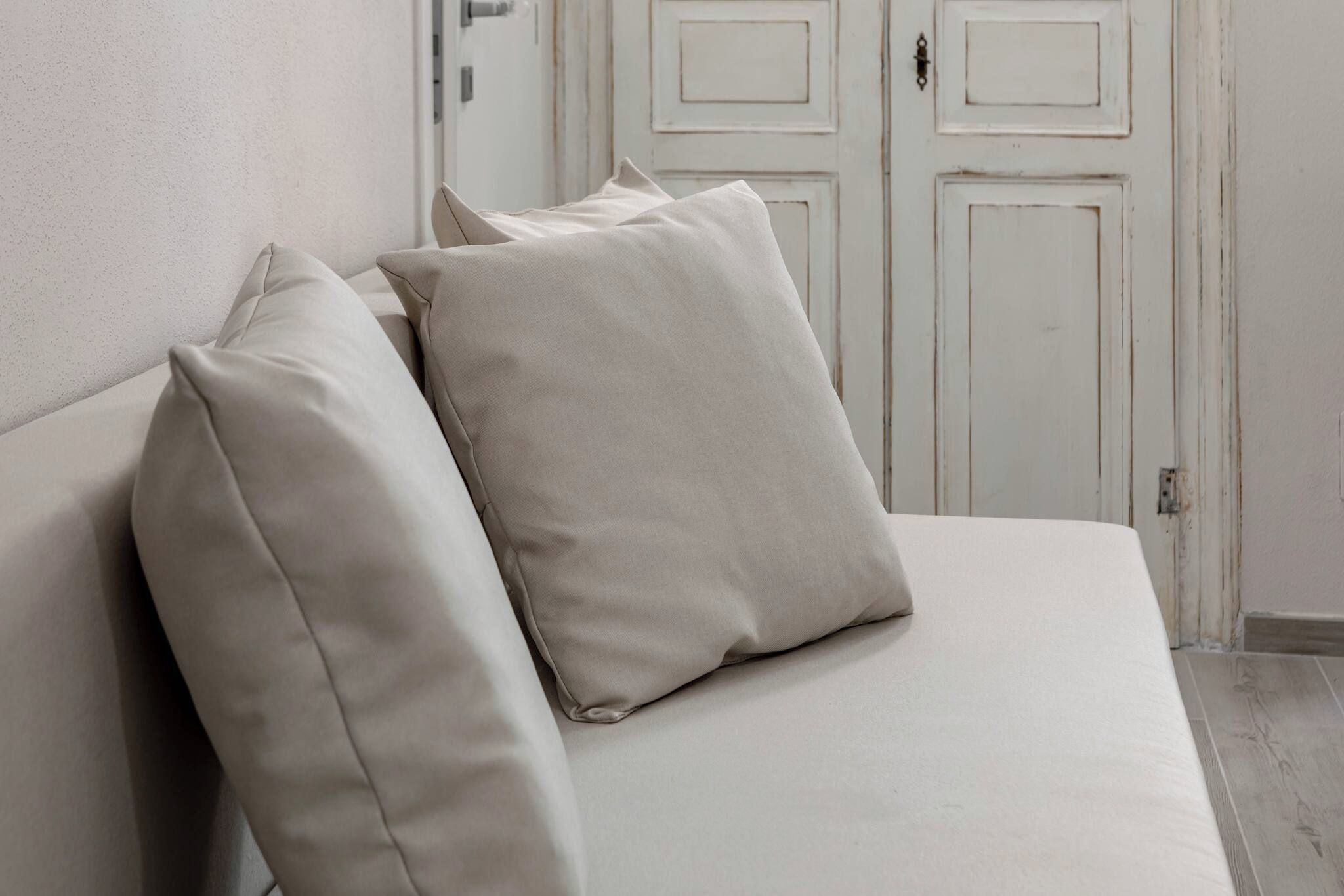 A bed with a white mattress and two pillows, a white wall, and a door in the background.