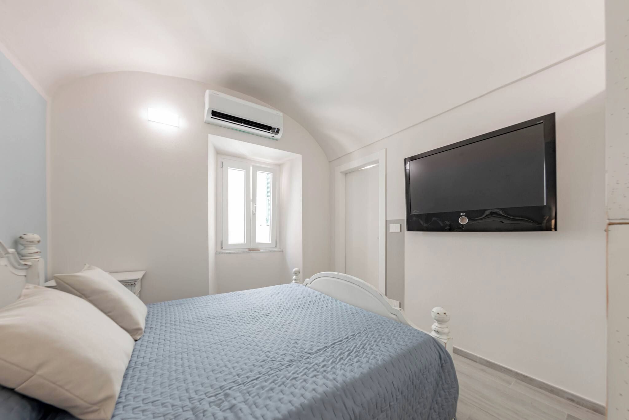 Une chambre à coucher comprenant un lit, une fenêtre, un appareil de climatisation et un téléviseur à écran plat fixé au mur.