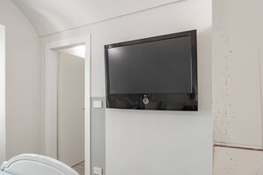 Una habitación con una televisión de pantalla plana montada en la pared, una puerta que da a otra estancia, y una bañera blanca al frente.