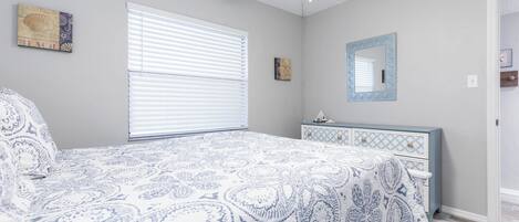 Un dormitorio con una cama, un aparador, una ventana con persianas y un ventilador de techo.
