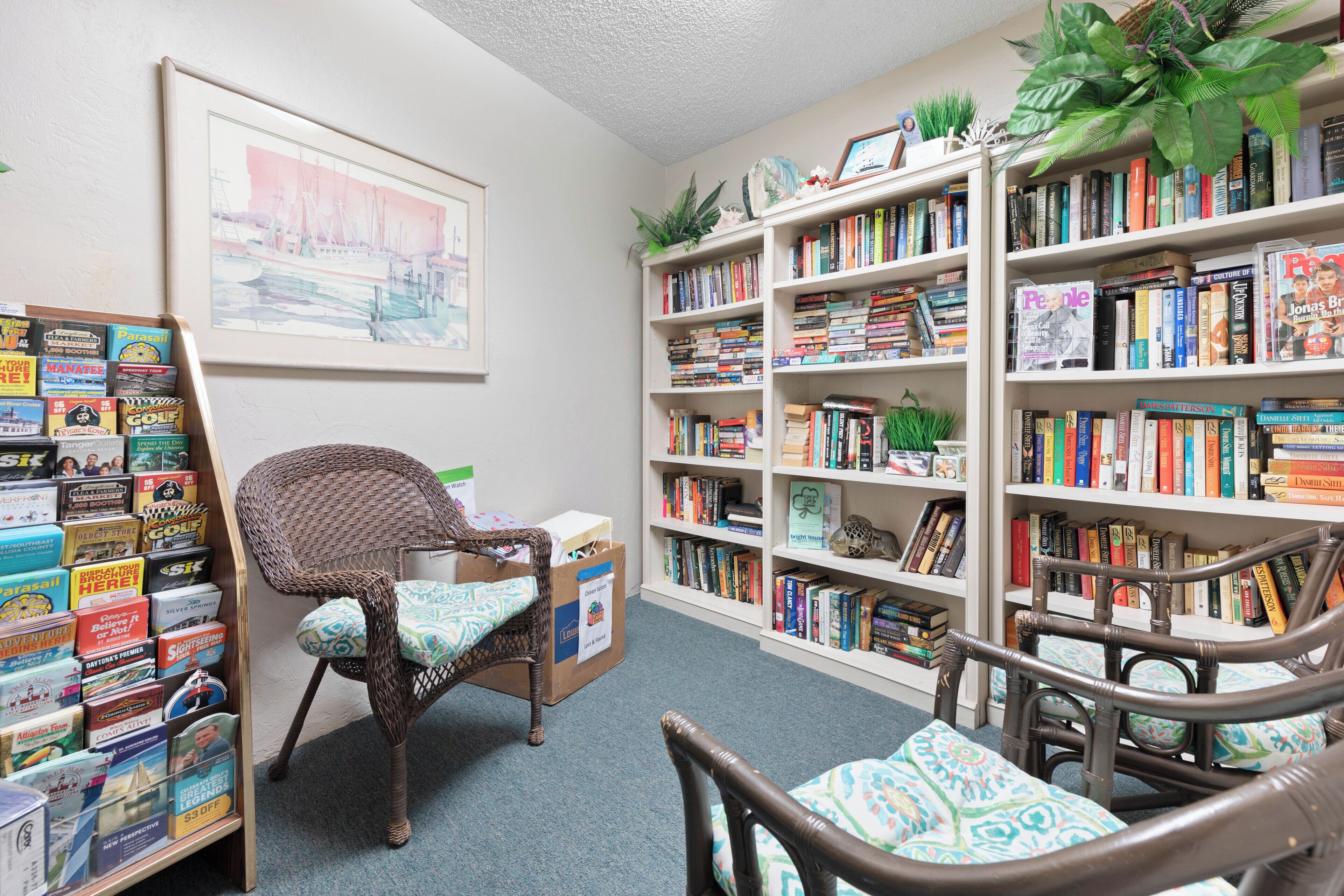 Une bibliothèque avec des étagères, des fauteuils en osier et un tableau encadré au mur.