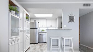 A modern kitchen with white cabinetry, a stainless steel refrigerator, and a built-in dishwasher. - Ocean Watch Oasis Monthly Beach Front Retreat (Ormond Beach)