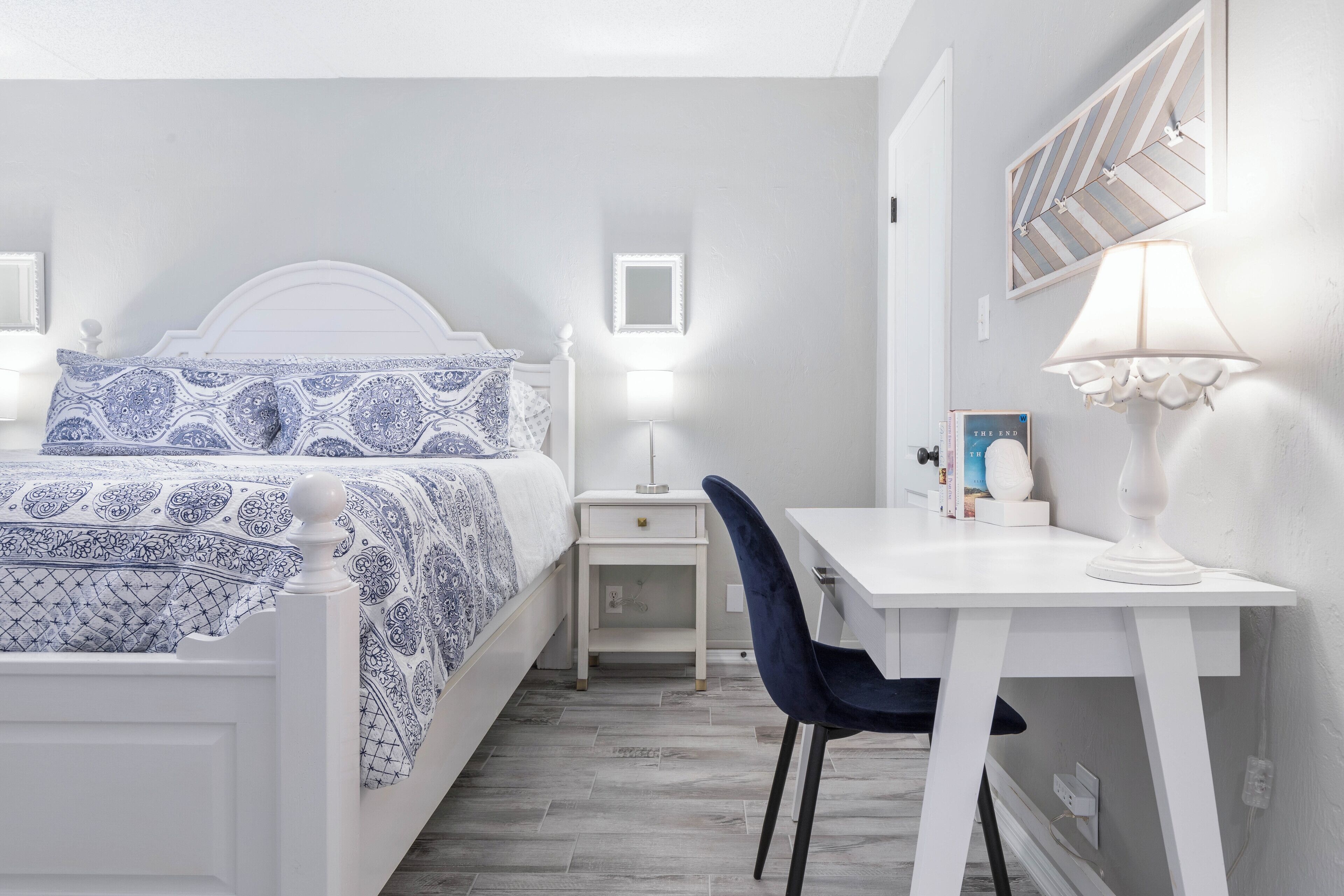 Ein Schlafzimmer mit Bett, Nachttisch, Stuhl, Schreibtisch, Lampe und Wanddekoration.