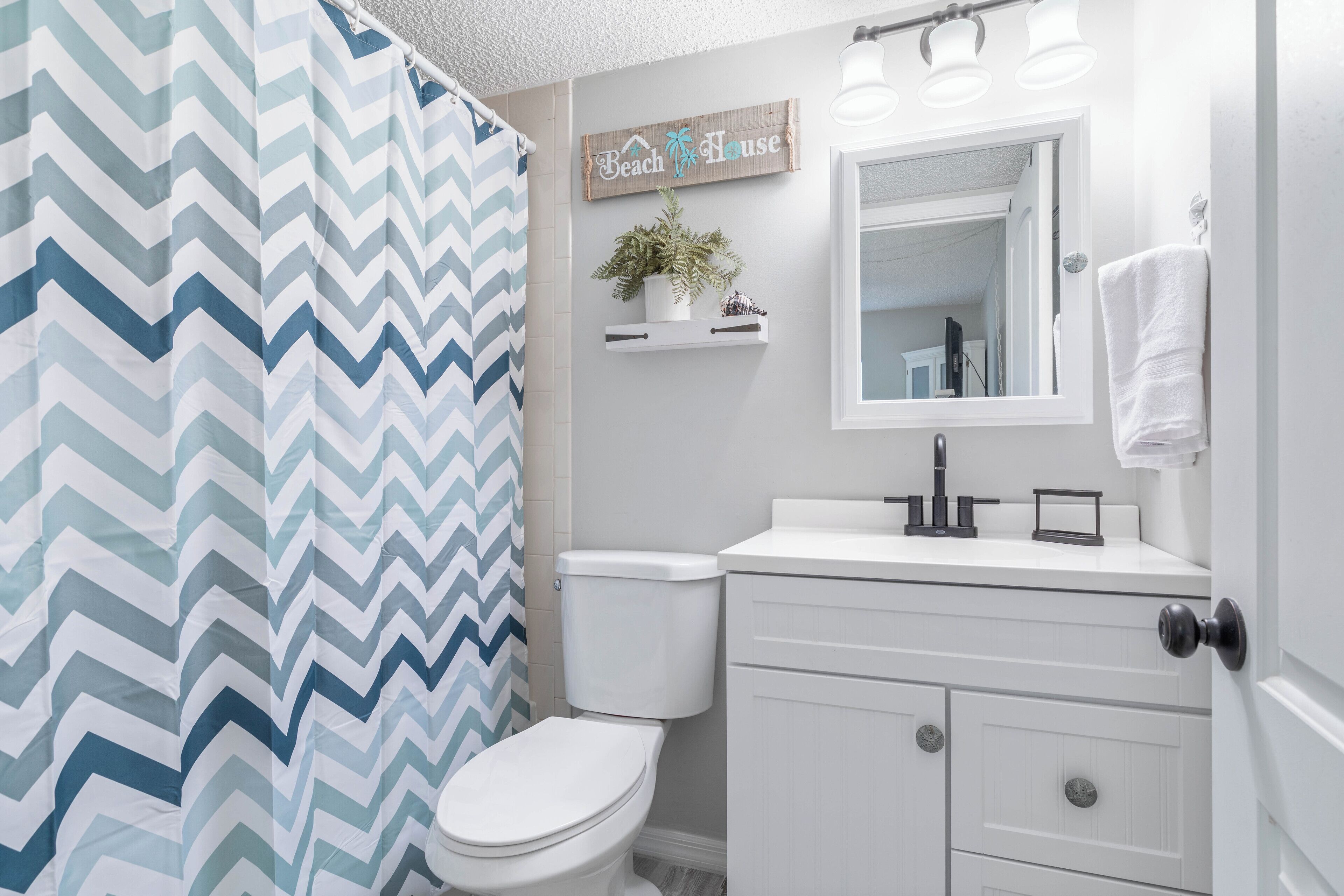 A bathroom with a white toilet, a white sink with a mirror above it, and a shower curtain with a chevron pattern.