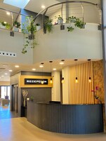 Un área de recepción moderna con un cartel que dice “RECEPTION”, una escalera curva y plantas en macetas.