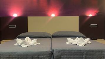 Een tweepersoonsbed met een grijs geborduurde spreideken en twee witte handdoeken erover gevouwen.