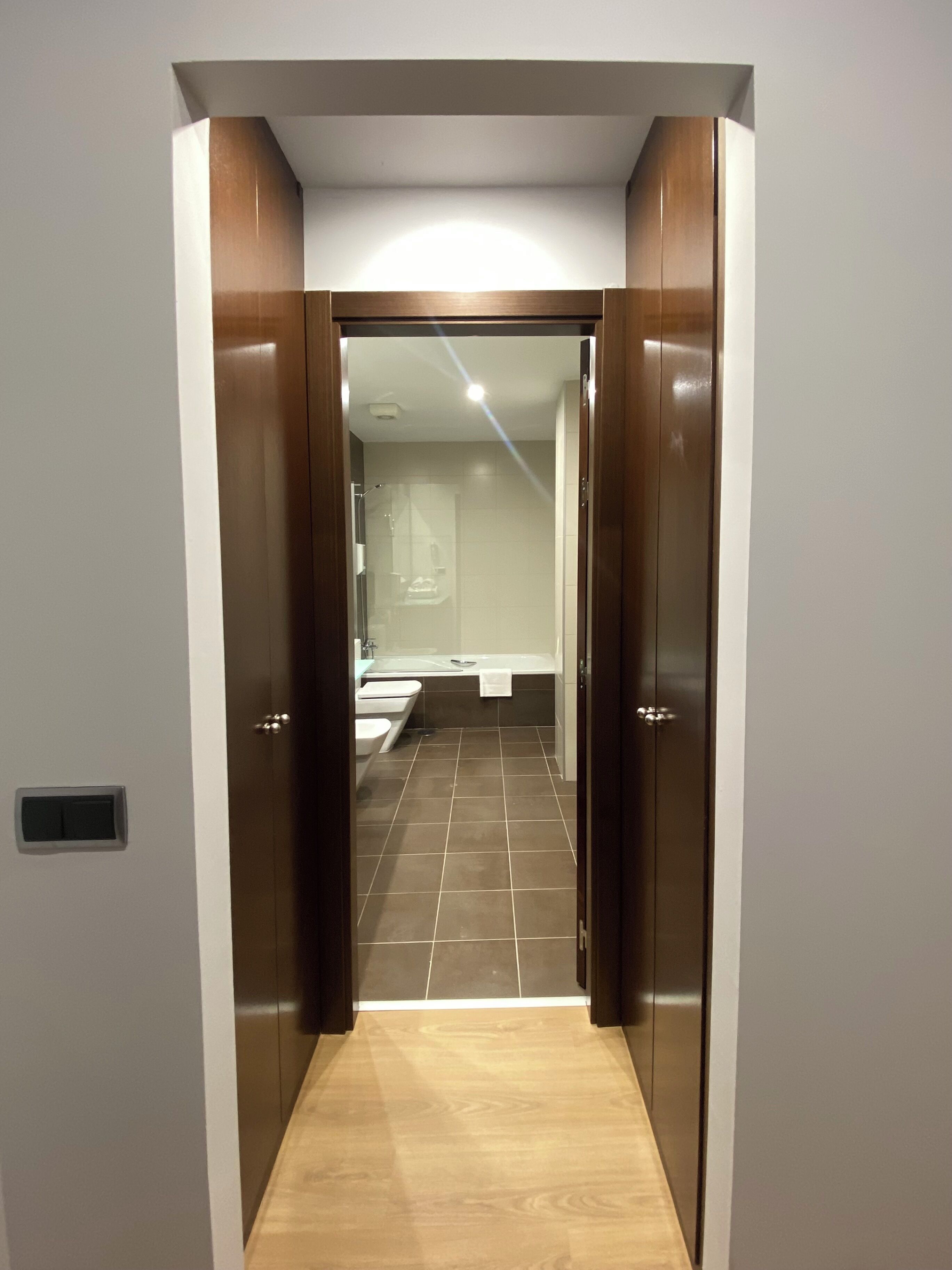 Un couloir menant à une salle de bain équipée d’une douche, d’un lavabo et de toilettes.