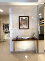 Una zona de recepción con un cuadro enmarco de un castillo, una consola de madera con un cuenco blanco y una piña, y una pequeña jaula de pájaros.